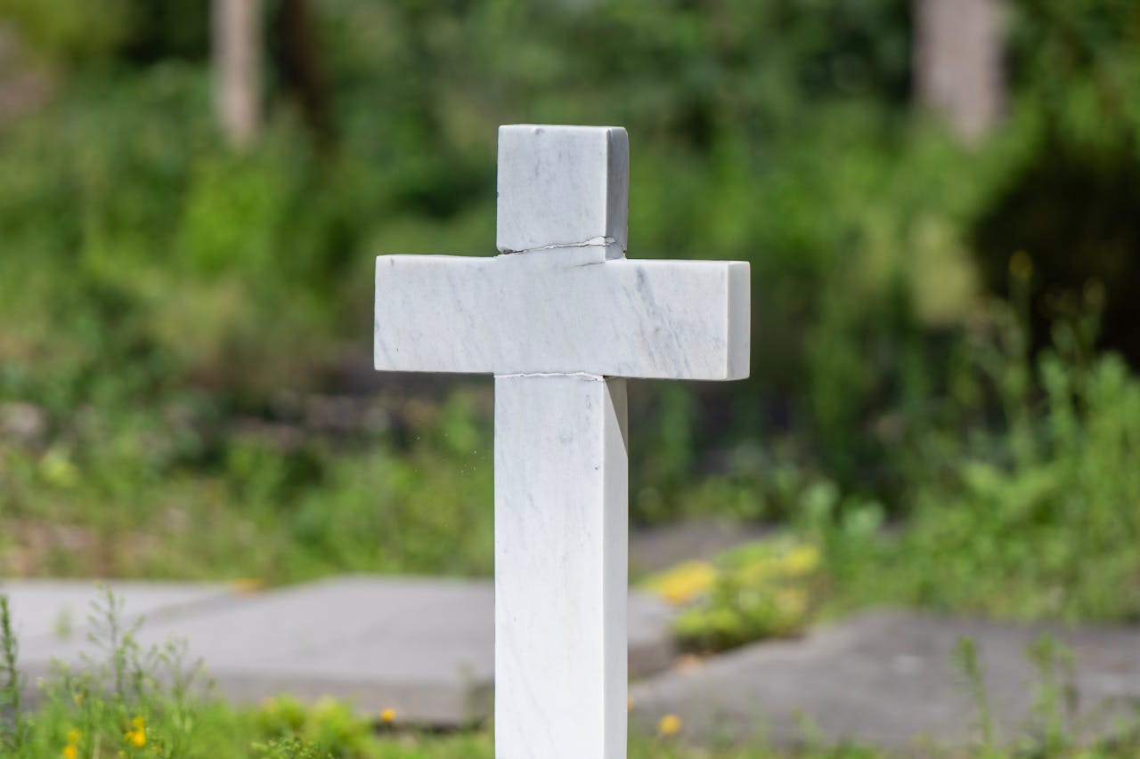 gallery-3 A serene marble cross in a lush green cemetery, symbolizing peace and remembrance.