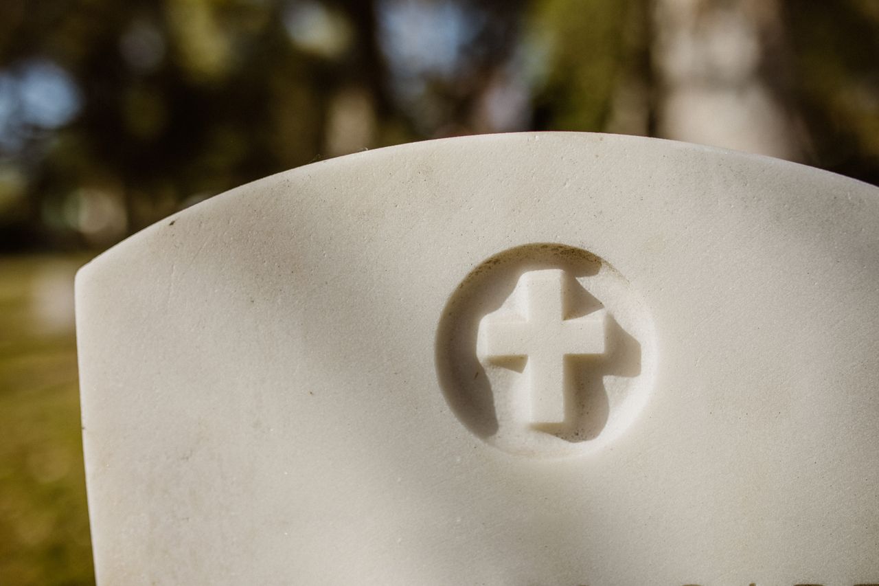 ours-journey A detailed view of a carved cross on a marble tombstone in a cemetery.